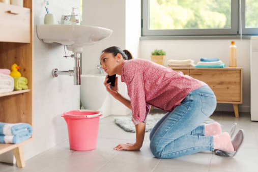 Woman calling a professional plumber at home using her smartphone, her bathroom sink is leaking